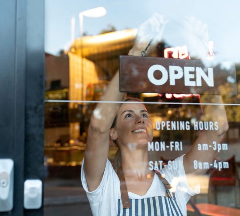 A shop owner hanging an Open sign in her window